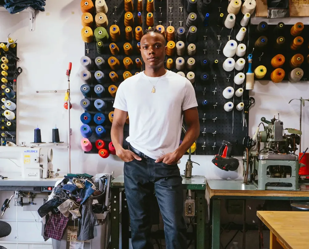 A maker standing in a workshop hung with spools of thread.