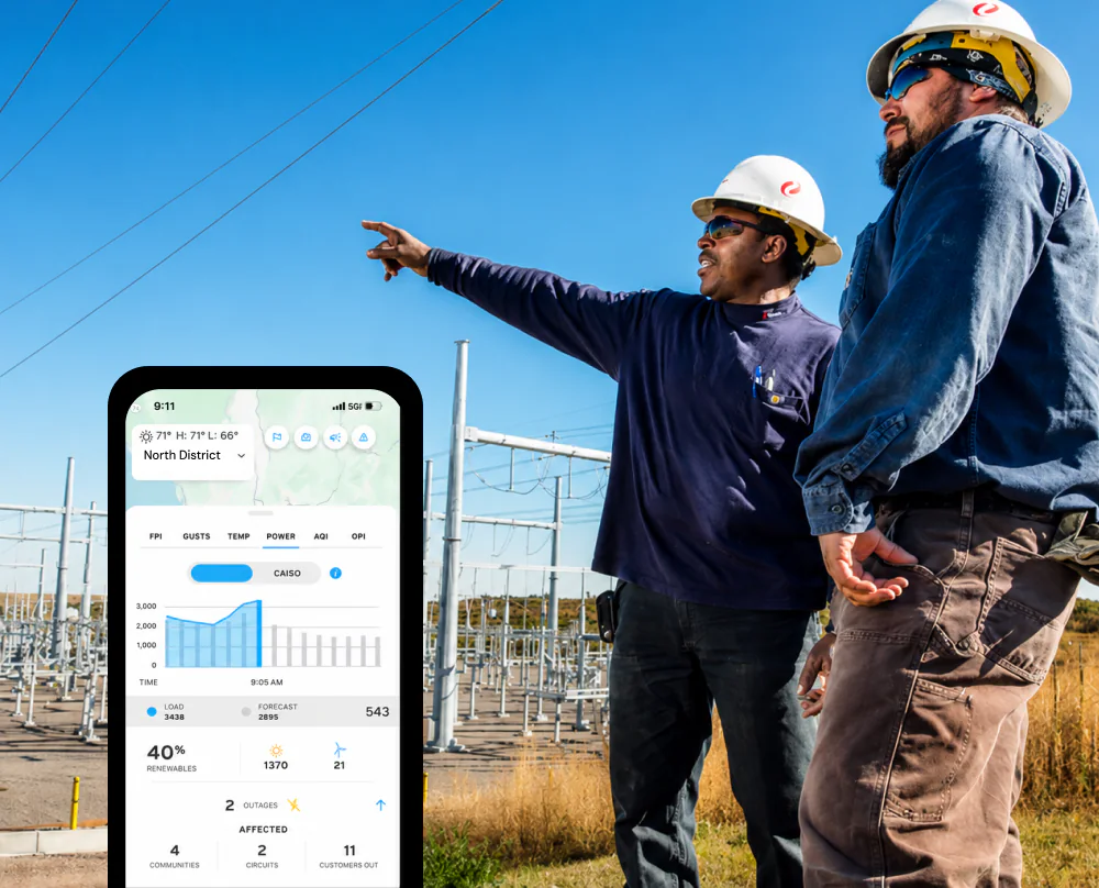 Two utility field workers at a substation, one pointing across the site, with the weather intelligence platform open on a phone.