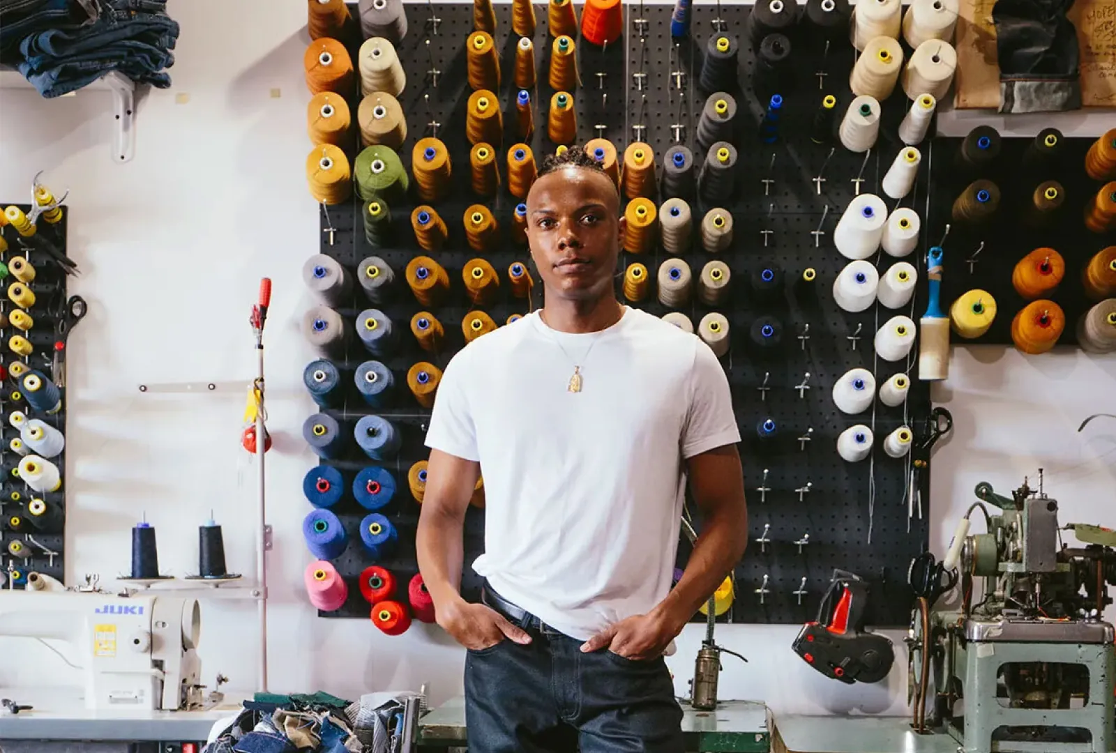 A maker in a workshop hung with spools of thread