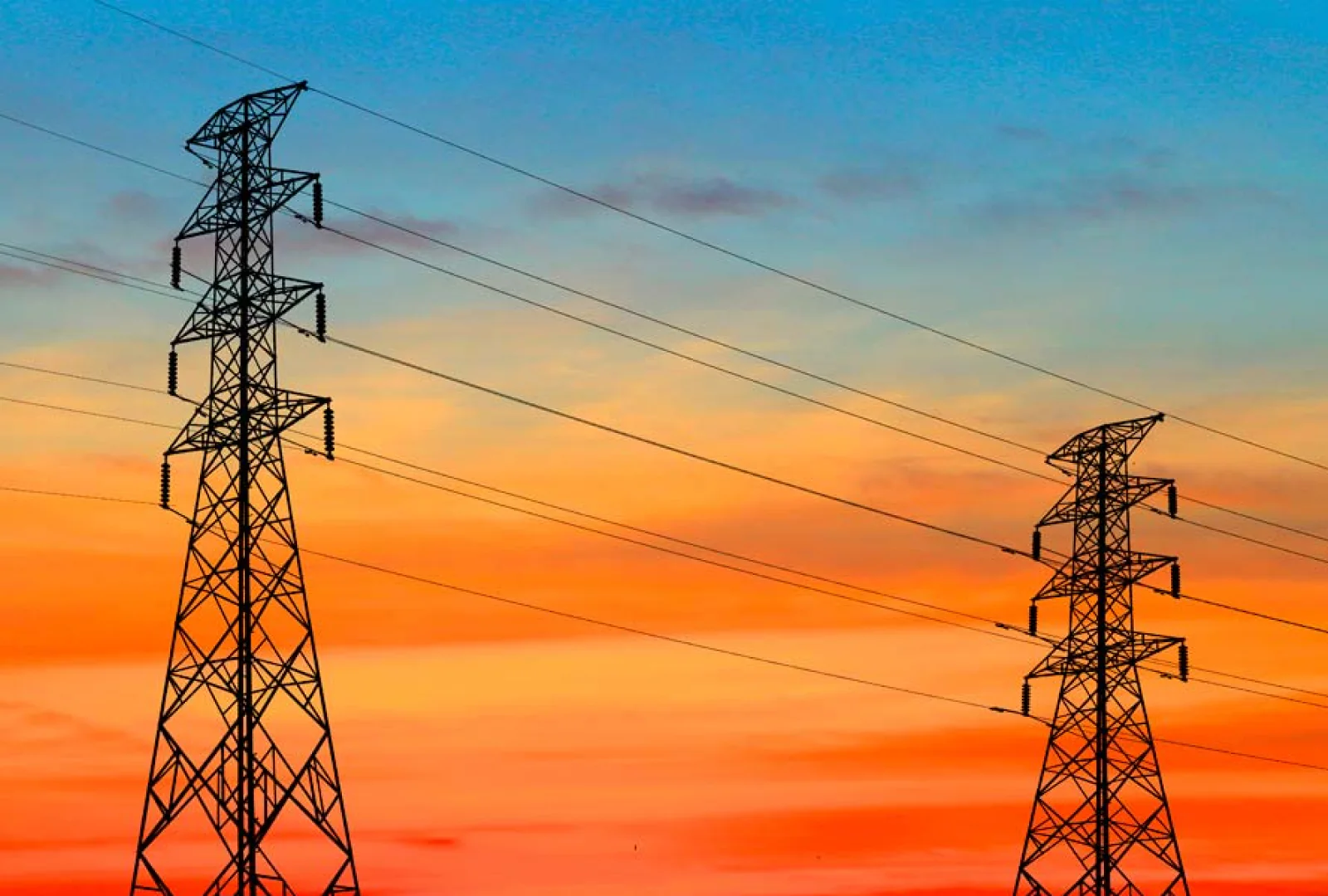 Electrical transmission towers silhouetted against a deep orange sunset sky.